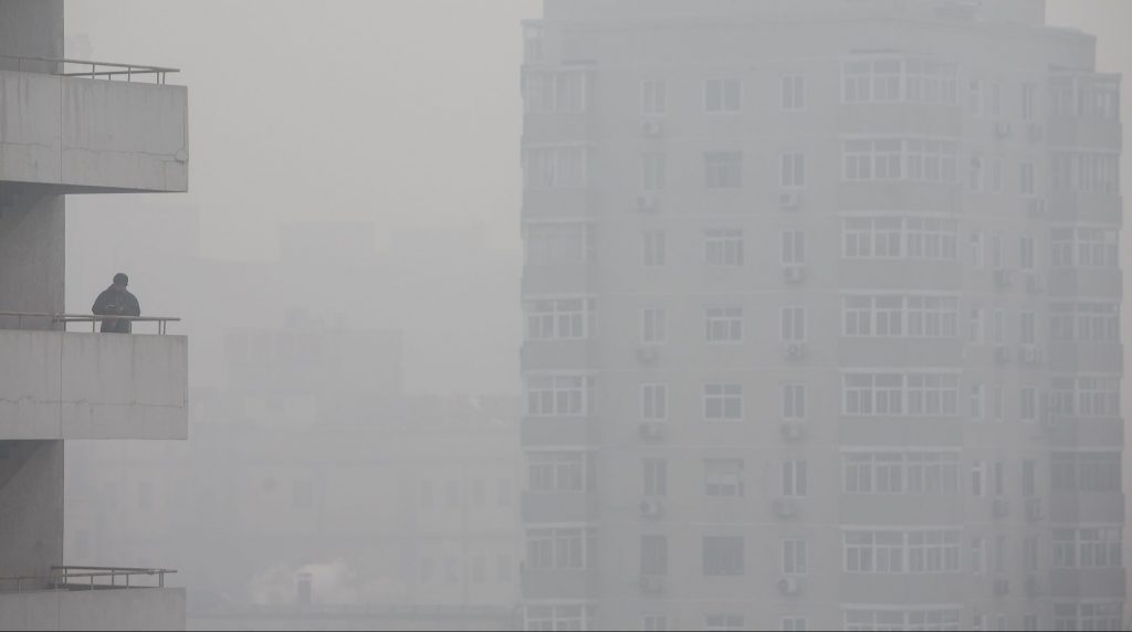 A man stands on a balcony as buildings stand shrouded in haze in Beijing, China, on Monday, Nov. 30, 2015. The round of air pollution that began last week is the heaviest of 2015, the Beijing environmental protection bureau said on its official microblog Tuesday. Photographer: Qilai Shen/Bloomberg via Getty Images