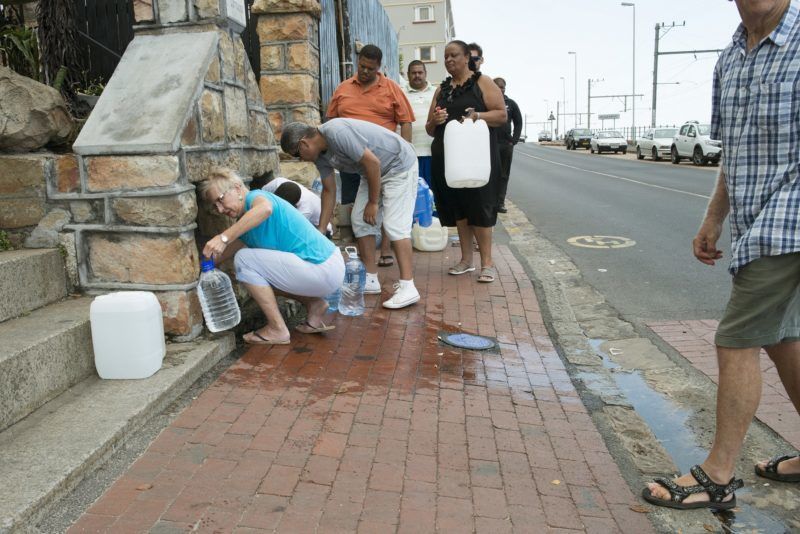 People collect drinking water from pipes fed by an underground spring, in St. James, about 25km from the city centre, on January 19, 2018, in Cape Town. 
Cape Town will next month slash its individual daily water consumption limit by 40 percent to 50 litres, the mayor said on January 18, as the city battles its worst drought in a century. / AFP PHOTO / RODGER BOSCH
