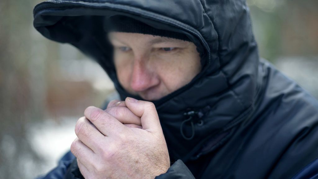 Man wearing hood warming his hands, outdoor horizontal shot