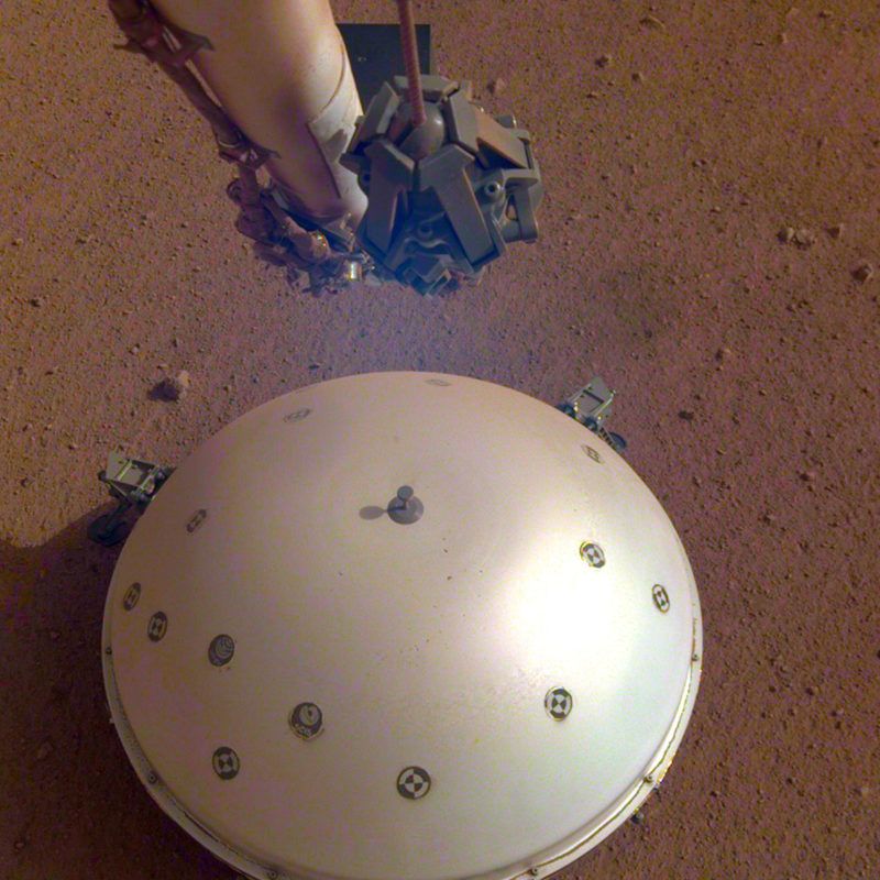 Világûr, 2019. április 24.Az amerikai Országos Repülésügyi és Ûrkutatási Hivatal, a NASA által 2019. április 23-án közreadott kép a NASA InSight nevû Mars-szondájának hõpajzzsal védett szeizmométerérõl. A francia ûrkutatási ügynökség, a Cnes közleménye szerint április 6-án gyenge, de világosan észlelhetõ rengést érzékelt a Marson az amerikai ûrszonda. A Mars belsejének kutatása céljából május 5-én útjára indított InSight robotgeológus ûrszonda mintegy 485 ezer kilométernyi út megtétele után 2018. november 26-án landolt a vörös bolygón.MTI/AP