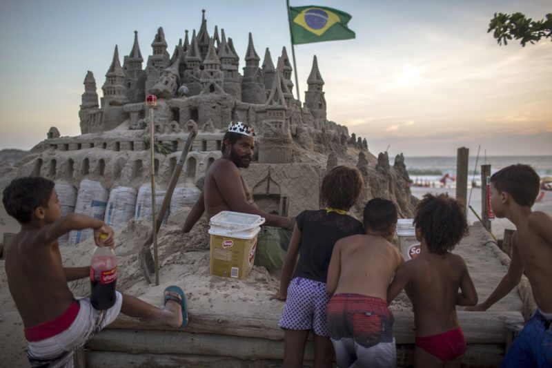 With a crown on his head, Marcio Mizael Matolias, 44, speaks with children who are interested in his sand castle, at Barra da Tijuca beach in Rio de Janeiro, Brazil, on January 18, 2018. 
For the last 22 years, Matolias has lived inside his sand castle surrounded by books, golf clubs and fishing poles. Neighbors and friends call him "The King".  / AFP PHOTO / MAURO PIMENTEL