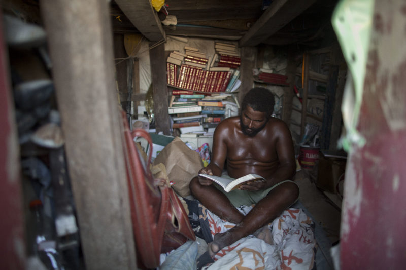 Marcio Mizael Matolias reads a book inside his sand castle, where he lives on the beach of Barra da Tijuca in Rio de Janeiro, Brazil, on January 18, 2018. 
For the last 22 years, Matolias has lived inside his sand castle surrounded by books, golf clubs and fishing poles. Neighbors and friends call him "The King".  / AFP PHOTO / MAURO PIMENTEL
