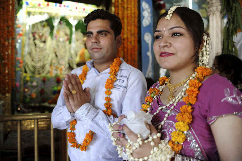 Newly wedded Indian couple Sapna (R) and her husband Amit (C) gestures after taking the blessing of Hindu God Lord Krishna during celebrations of the Teej Festival in the Sawan Month at The Durgiana Temple in Amritsar on July 24, 2011. The festival which heralds the rainy season, is essentially a women's festival and revolves around dressing in finery, singing and dancng.   AFP PHOTO/NARINDER NANU (Photo by NARINDER NANU / AFP)